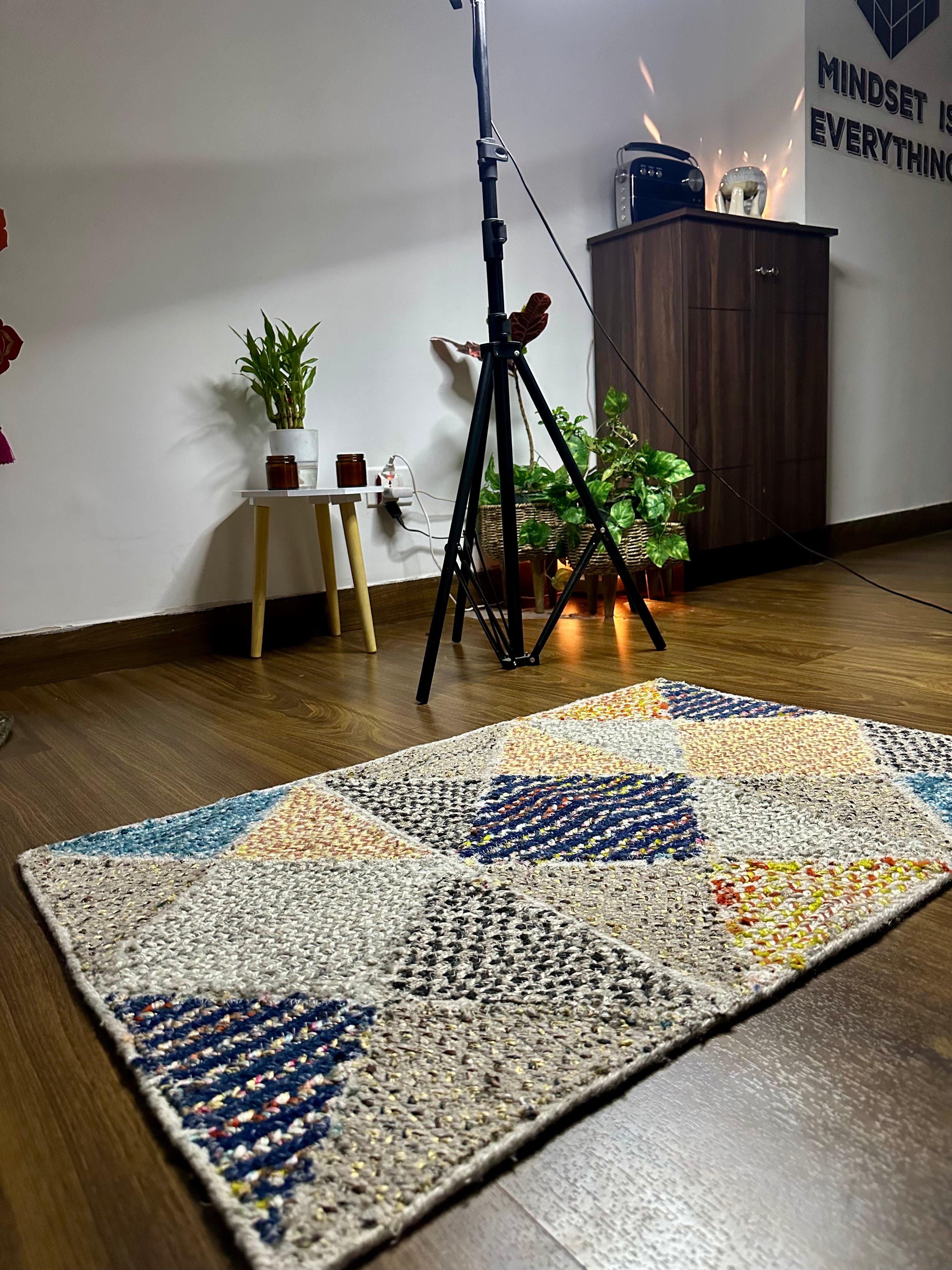Multicolored geometric-patterned rug on a wooden floor with camera equipment in the background.
